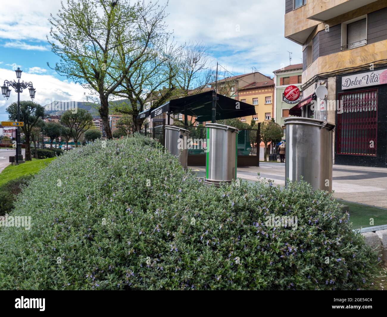 OVIEDO, SPANIEN - April 08, 2018: Getrennte garbage collection Metallic zylinderförmige Behälter auf der Straße hinter dekorative Bush Hedge, Oviedo, Spanien. Stockfoto