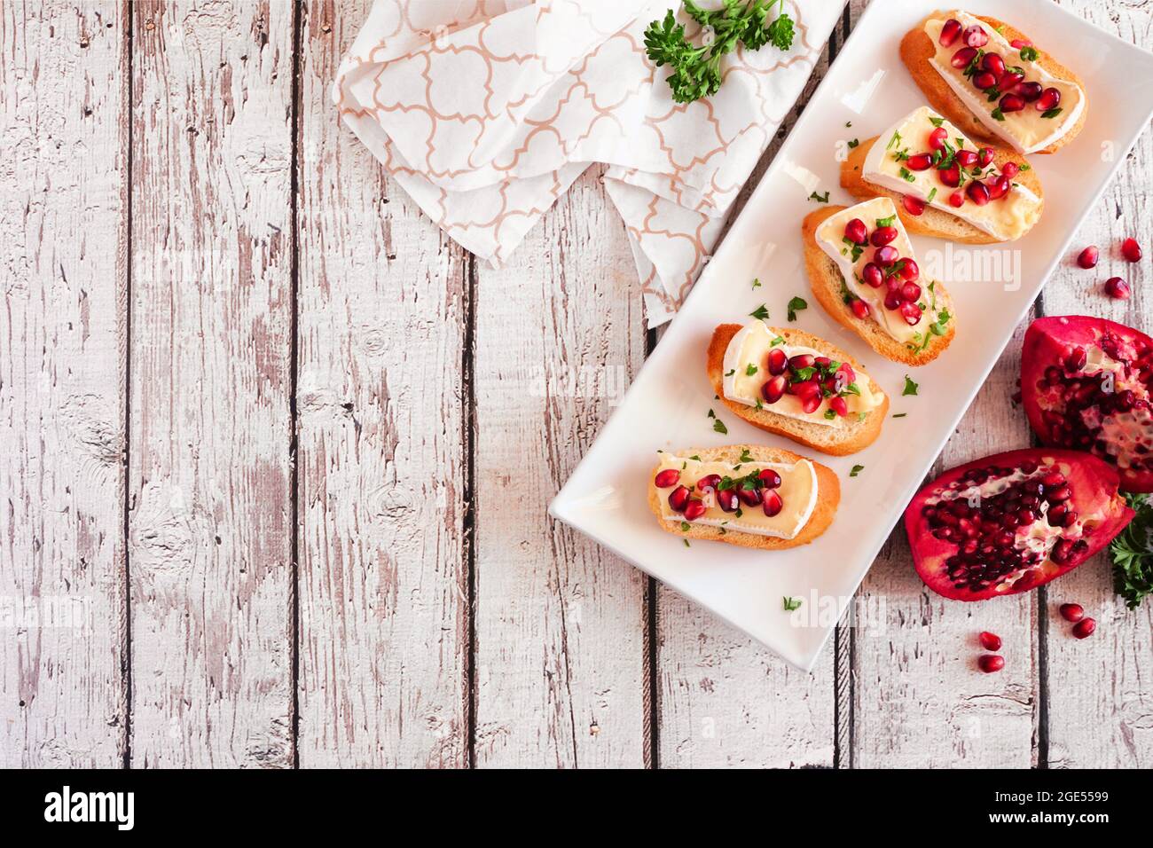 Holiday Crostini Vorspeisen mit Brie-Käse, Granatäpfel und Petersilie. Oben Tischszene auf weißem Holzhintergrund mit Kopierfläche. Party Stockfoto