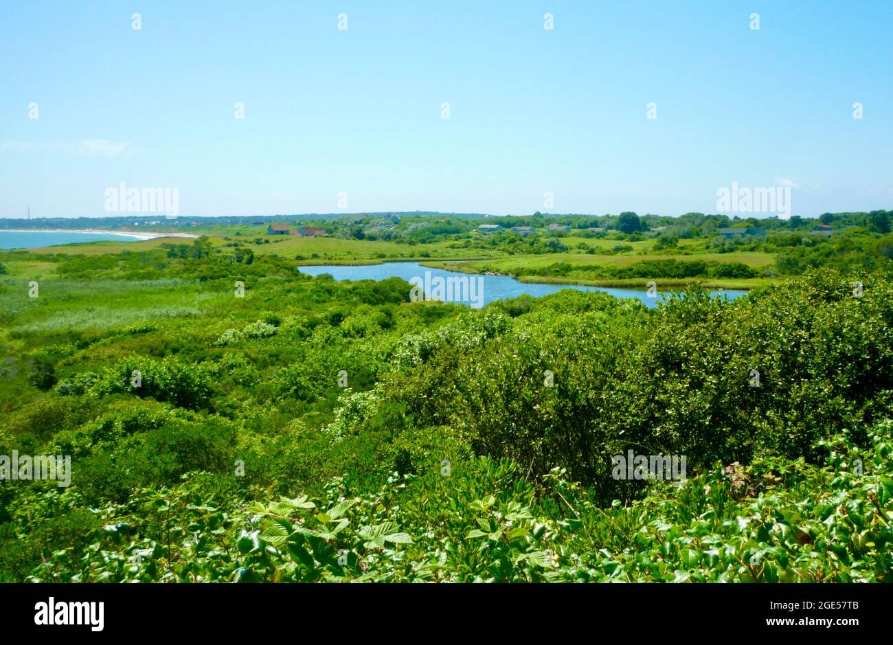 Ein Wanderweg auf Block Island blickt auf eine grüne Landschaft aus Sommerfeldern, Sträuchern und einer Binnenschifffahrt mit dem Atlantischen Ozean in der Ferne. Stockfoto