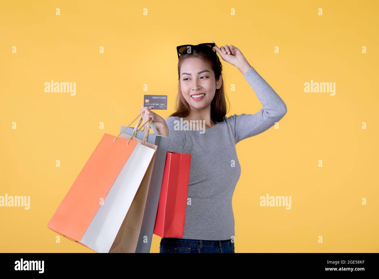 Glückliche asiatische Frau mit Einkaufstaschen und Kreditkarte lächelnd auf gelbem Hintergrund, leerem Raum Stockfoto