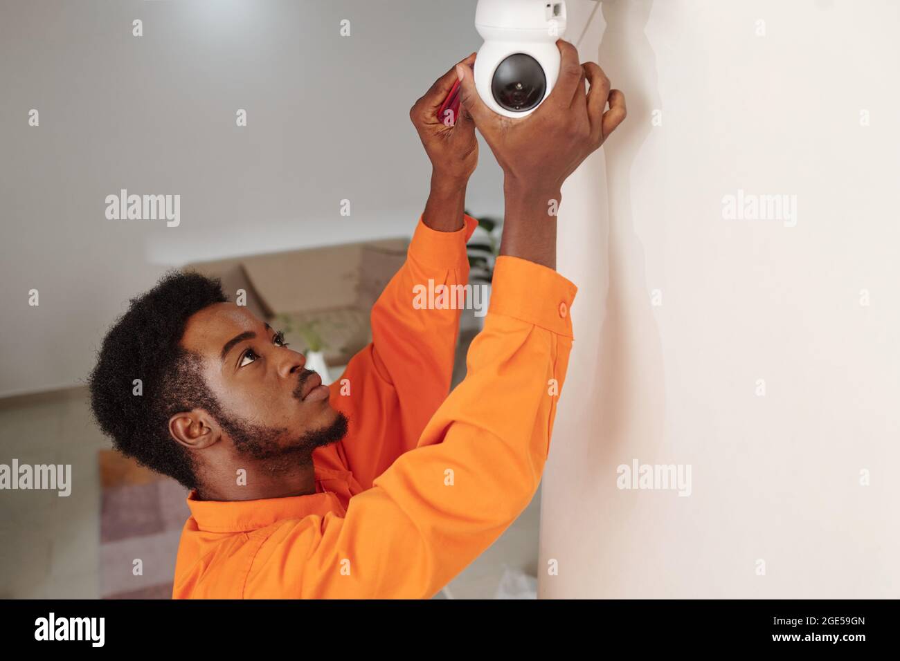Techniker in orangefarbener Uniform installiert Videoüberwachung im Bürogebäude Stockfoto