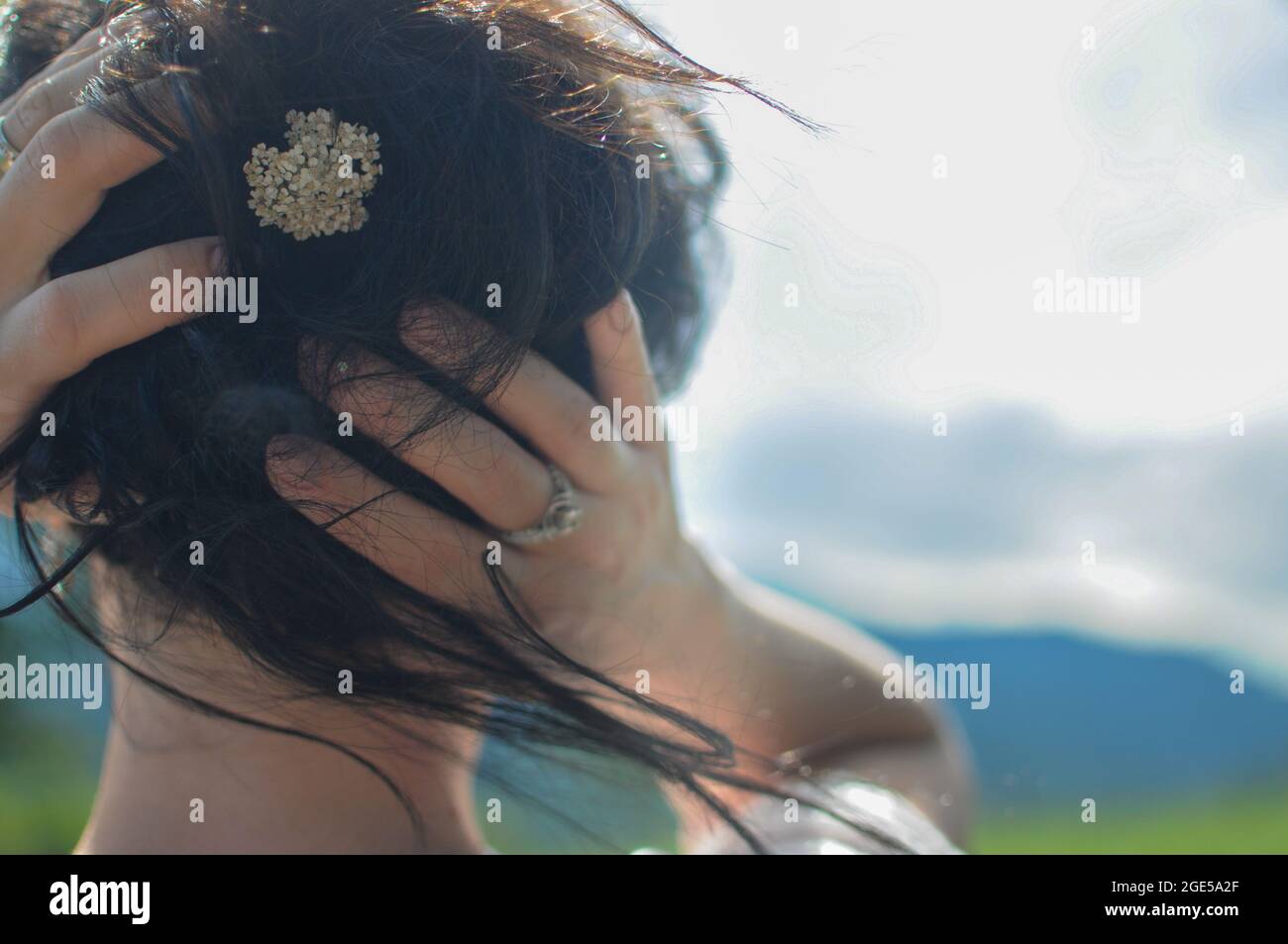 Ein Mädchen hält ihr Haar mit der kleinen Blume in der Hand. Natürliche Frisur Stockfoto