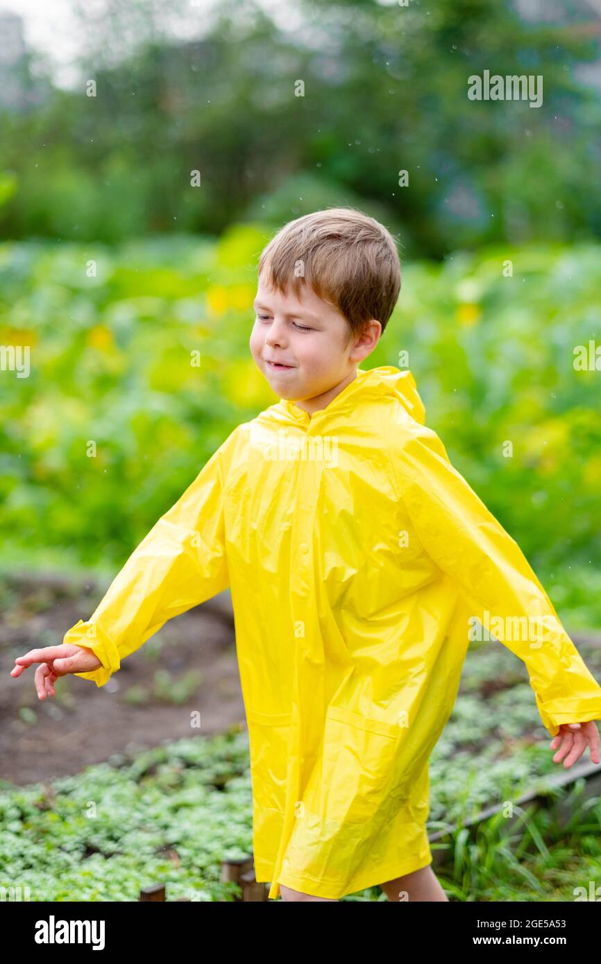 Ein Junge in einem gelben Regenmantel geht im Regen draußen. Schönes und lächelndes Kind auf der Straße. Helle Kleidung. Gehen Sie im Regen. Stockfoto