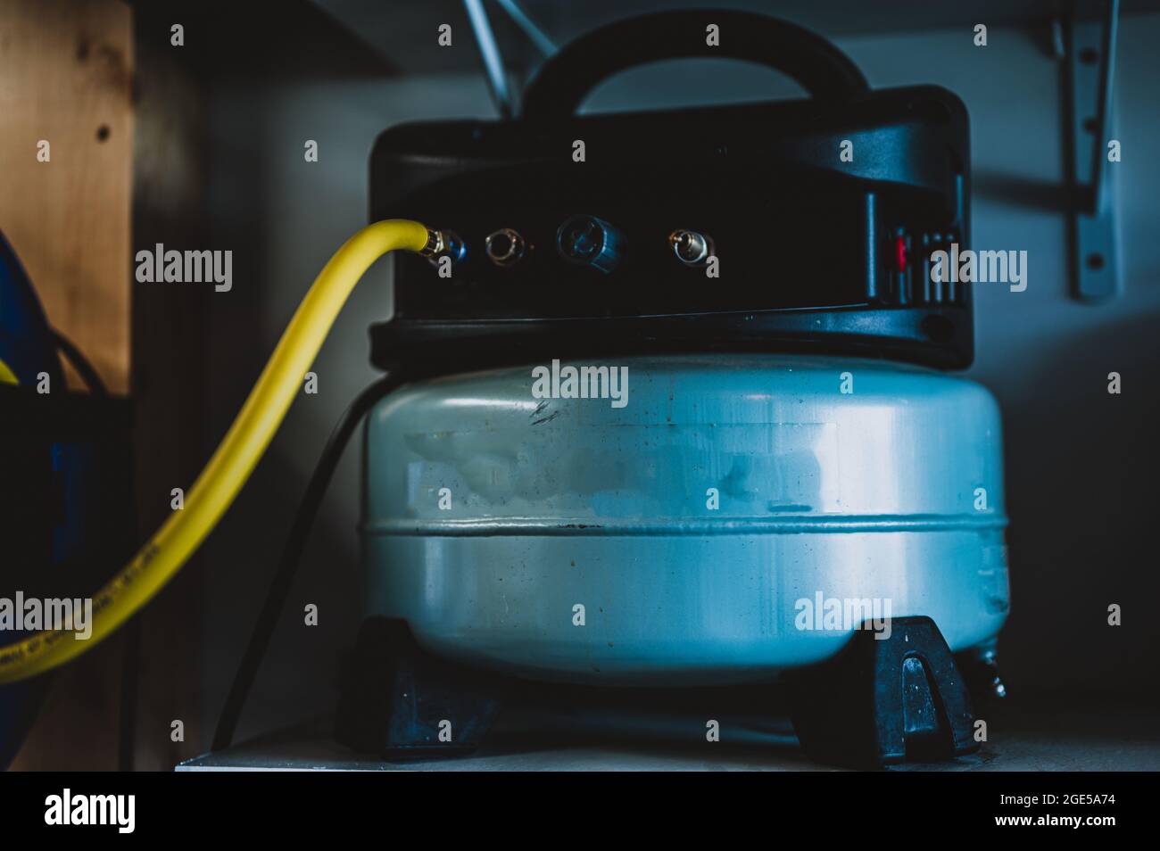 Konzentrieren Sie sich gezielt auf einen Schlauch, der mit einem Pfannkuchen-Luftkompressor verbunden ist, der auf einem Regal sitzt Stockfoto