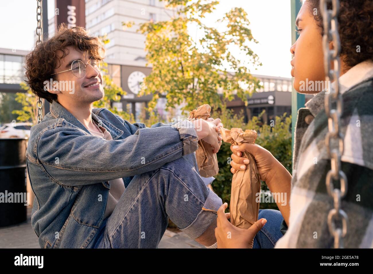 Lächelnder Teenager mit Flasche, der seine Freundin während der Diskussion im Freien ansieht Stockfoto