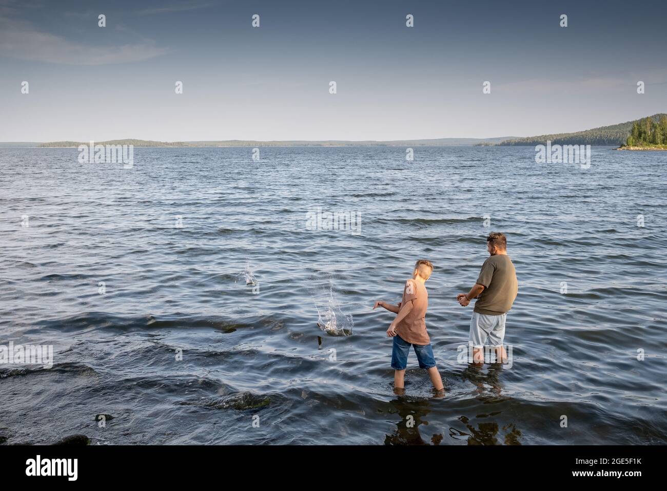 Junger Mann und Teenager, die am Sommertag im See stehen und Steine ins Wasser werfen Stockfoto