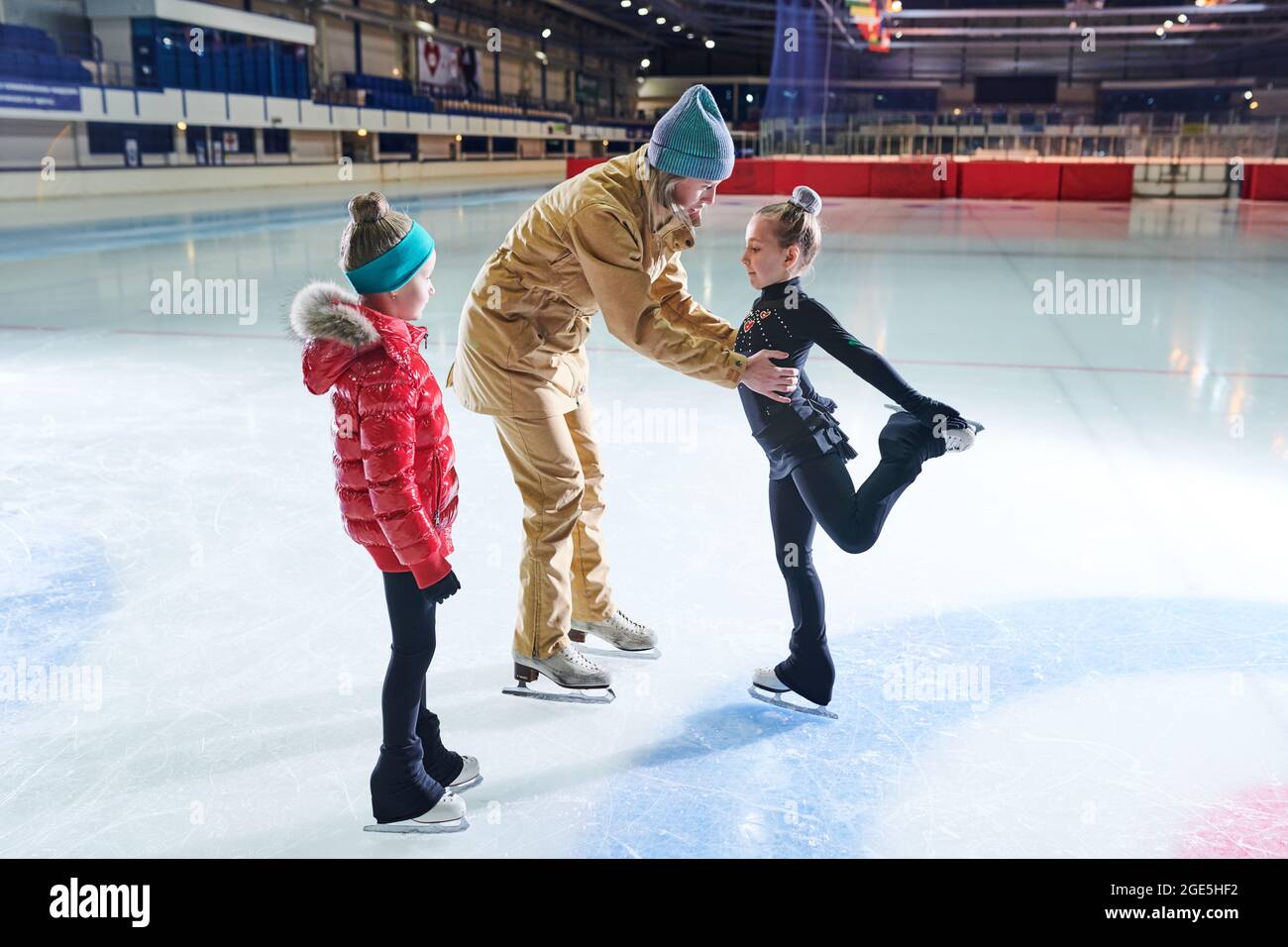 Portrait von zwei kleinen Mädchen, die beim Training mit einer Trainerin in der Halle Eislaufen lernen Stockfoto