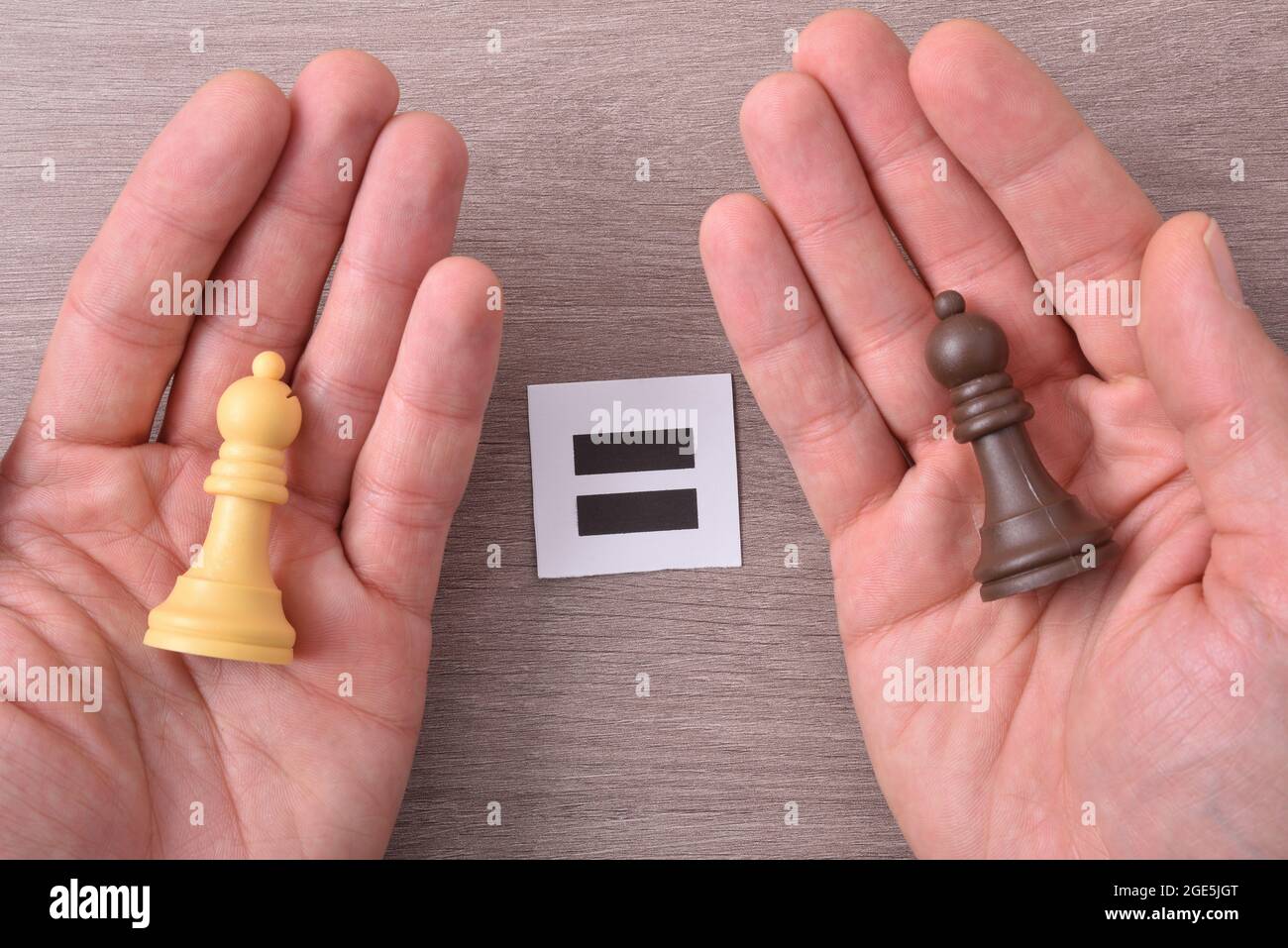 Multirassisches Gleichheitskonzept mit Händen mit verschiedenen farbigen Schachfiguren in jeder Hand auf Holztisch, der Zeichen mit gleichem Zeichen hält. Draufsicht. Stockfoto