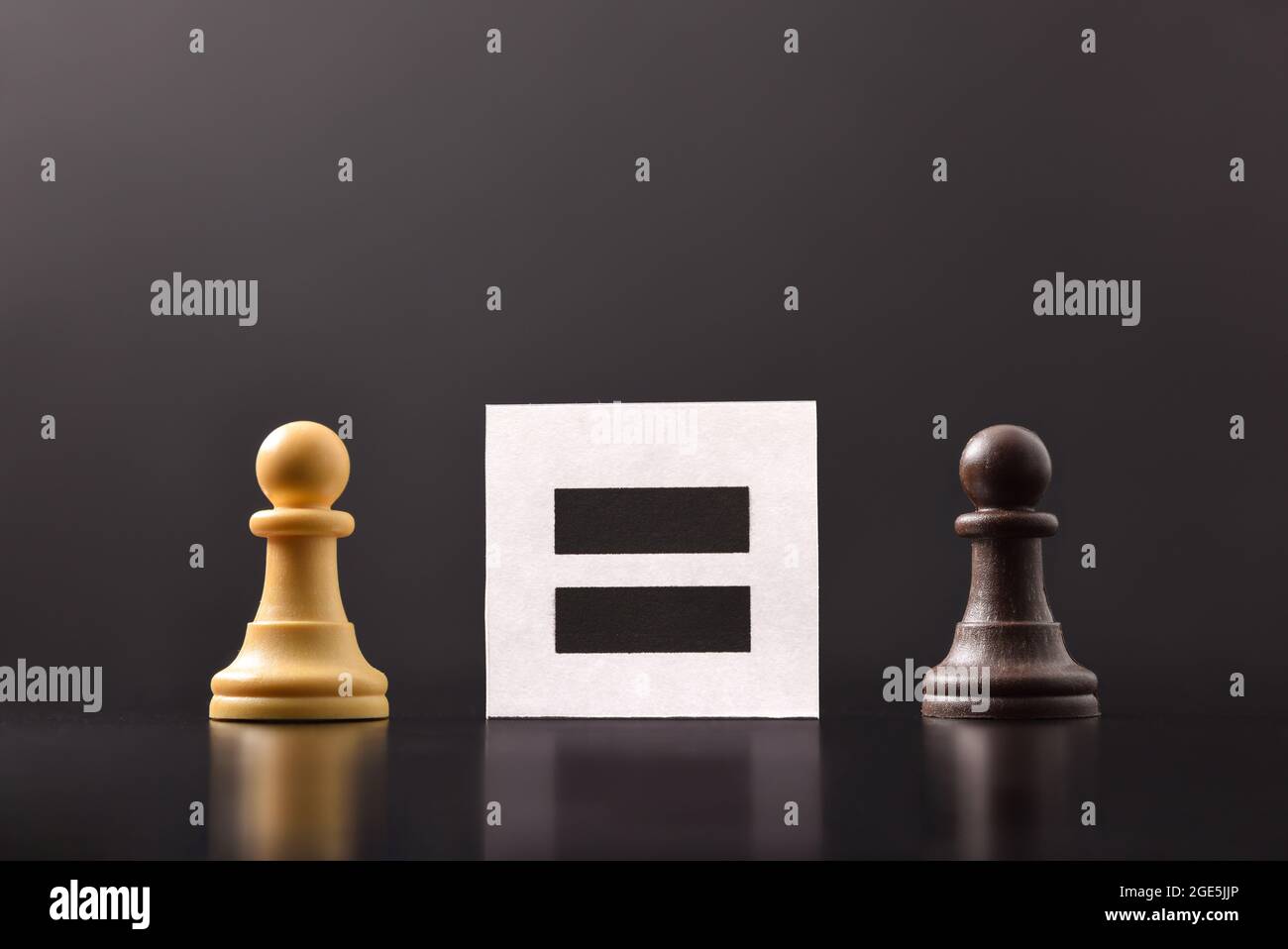 Konzept der Gleichheit zwischen Menschen mit schwarzen und weißen Schachfiguren mit dunklem Hintergrund und Plakat mit gleichem Zeichen Stockfoto