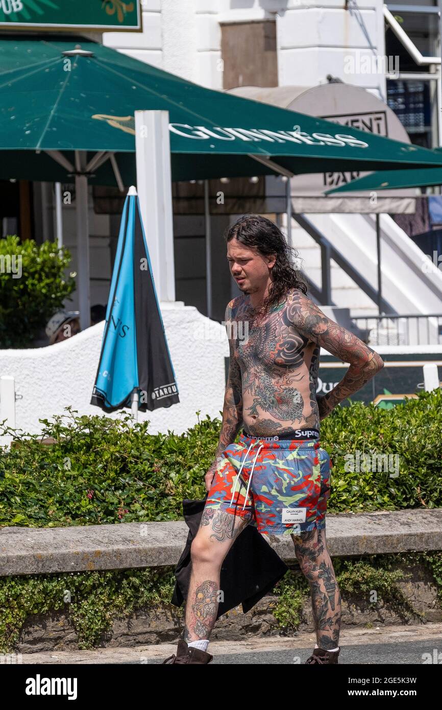 Ein junger Mann, schwer tätowiert mit japanischen Tattoos Irezumi, der in einem sonnigen Newquay Town Center in Cornwall spaziert. Stockfoto