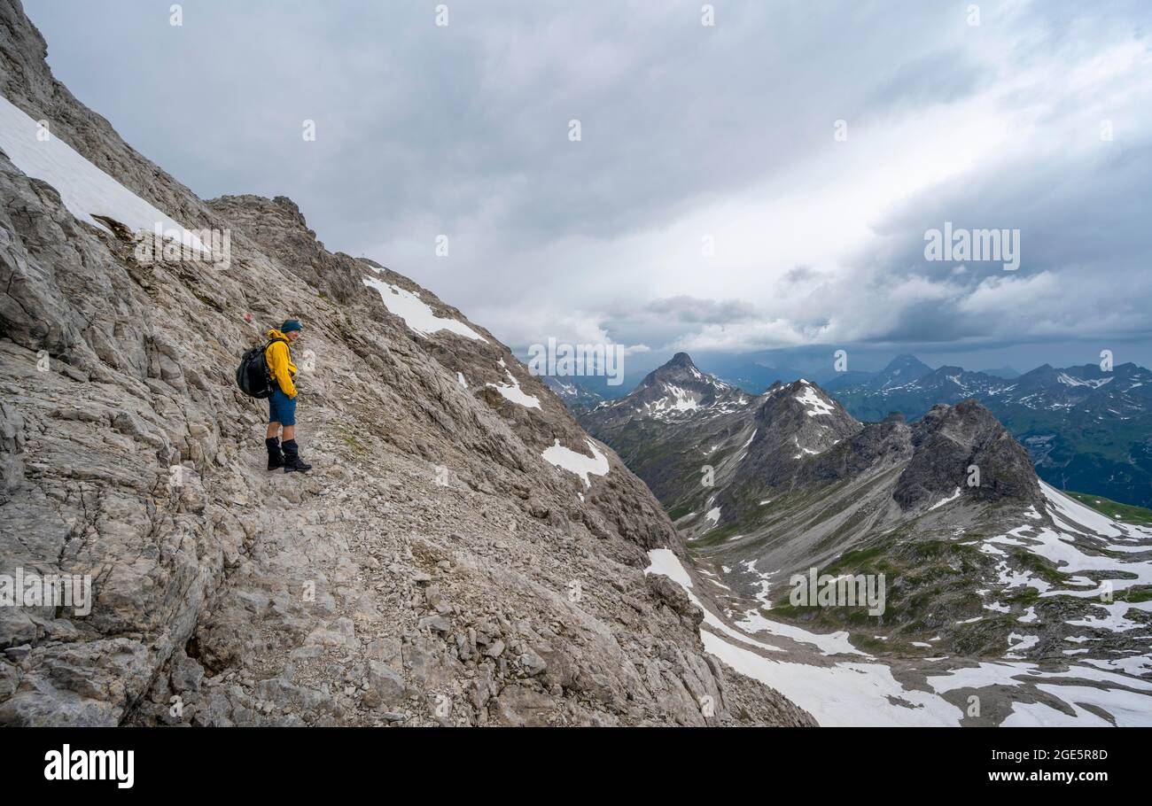 Wanderer auf Wanderweg in felsigem Gelände, Bergpanorama mit alten Schneefeldern und felsigen Berggipfeln im Hintergrund, dramatischer Wolkenhimmel Stockfoto