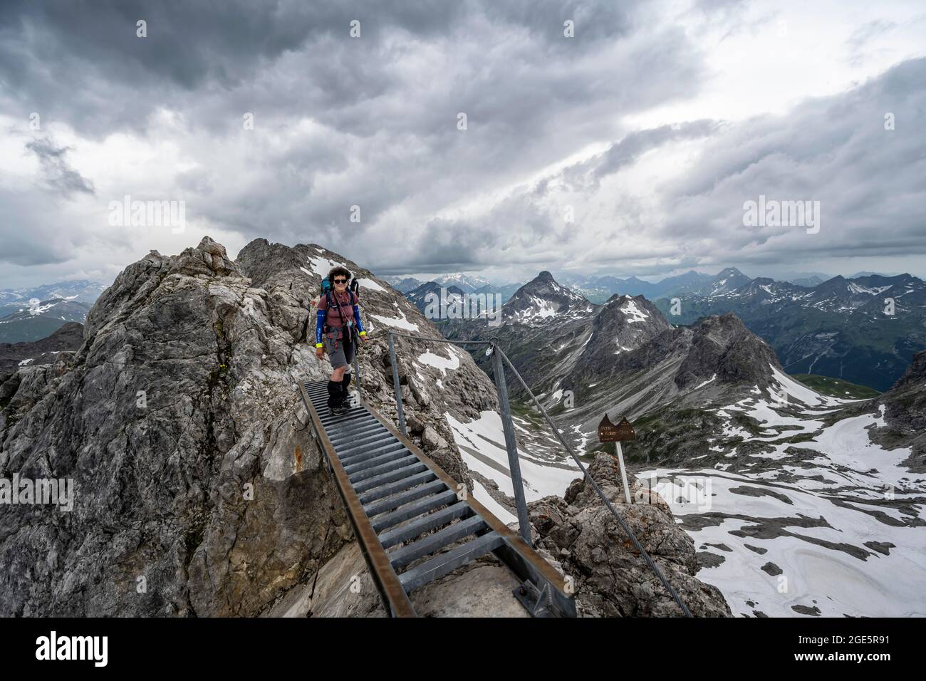 Wanderer auf einer Metallbrücke auf einem Felsen, Höhenweg mit Schneeresten, Bergpanorama mit hohem Licht, dramatischer Wolkenhimmel, Heilbronner Weg Stockfoto