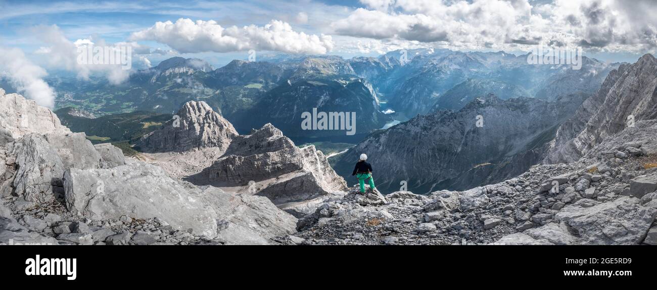 Wanderer mit Helm auf dem Gipfel des Watzmann Mittelgipfels, Blick über Berge, Königssee und Obersee, Wanderweg zum Watzmann, Watzmann Stockfoto