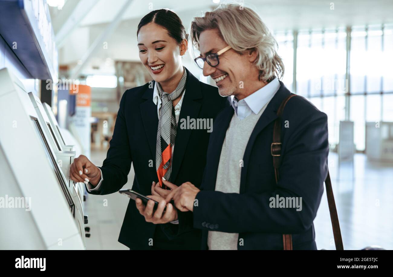 Freundlicher Bodenwächter, der männlichen Reisenden beim Check-in mit einem Automaten am Flughafenterminal behilflich ist. Geschäftsmann bei Selbstbedienungskontrolle Stockfoto