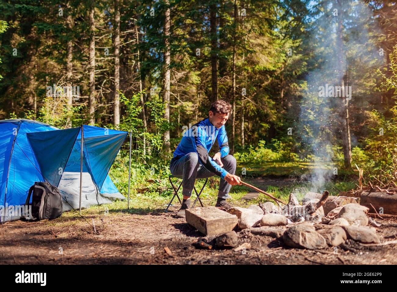 Mann, der am Lagerfeuer im Wald neben dem Zelt sitzt. Camping im Sommer. Allein reisen und die Natur genießen Stockfoto