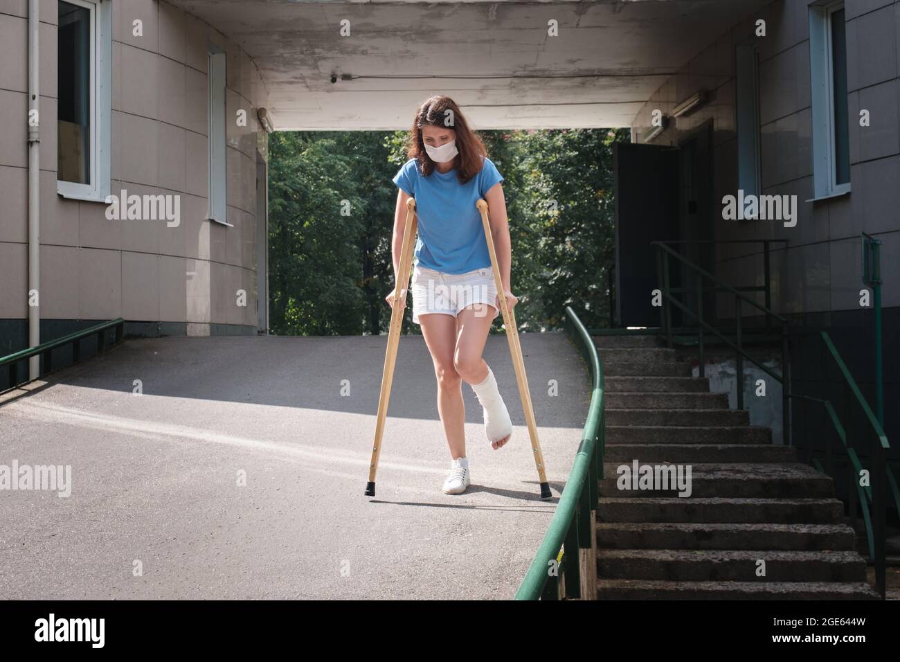 Eine Frau mit gebrochenem Bein geht mit orthopädischen Krücken eine Rampe hinunter. Stockfoto