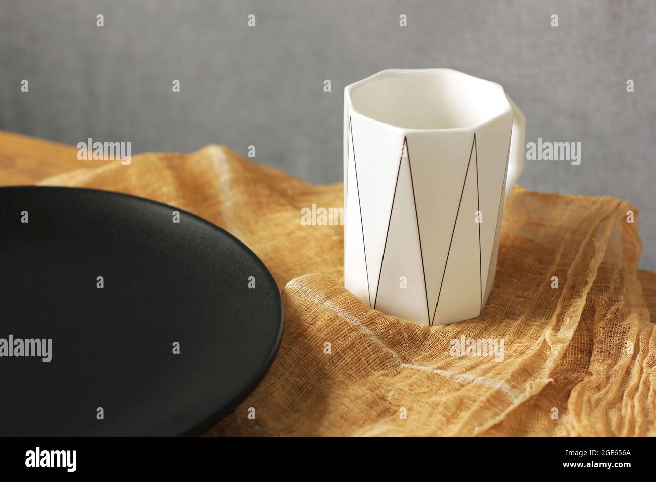 Leere schwarze Platte und weiße Tasse. Leeren Sie das Geschirr. Minimalistisches Geschirr. Teller ohne Lebensmittel Stockfoto