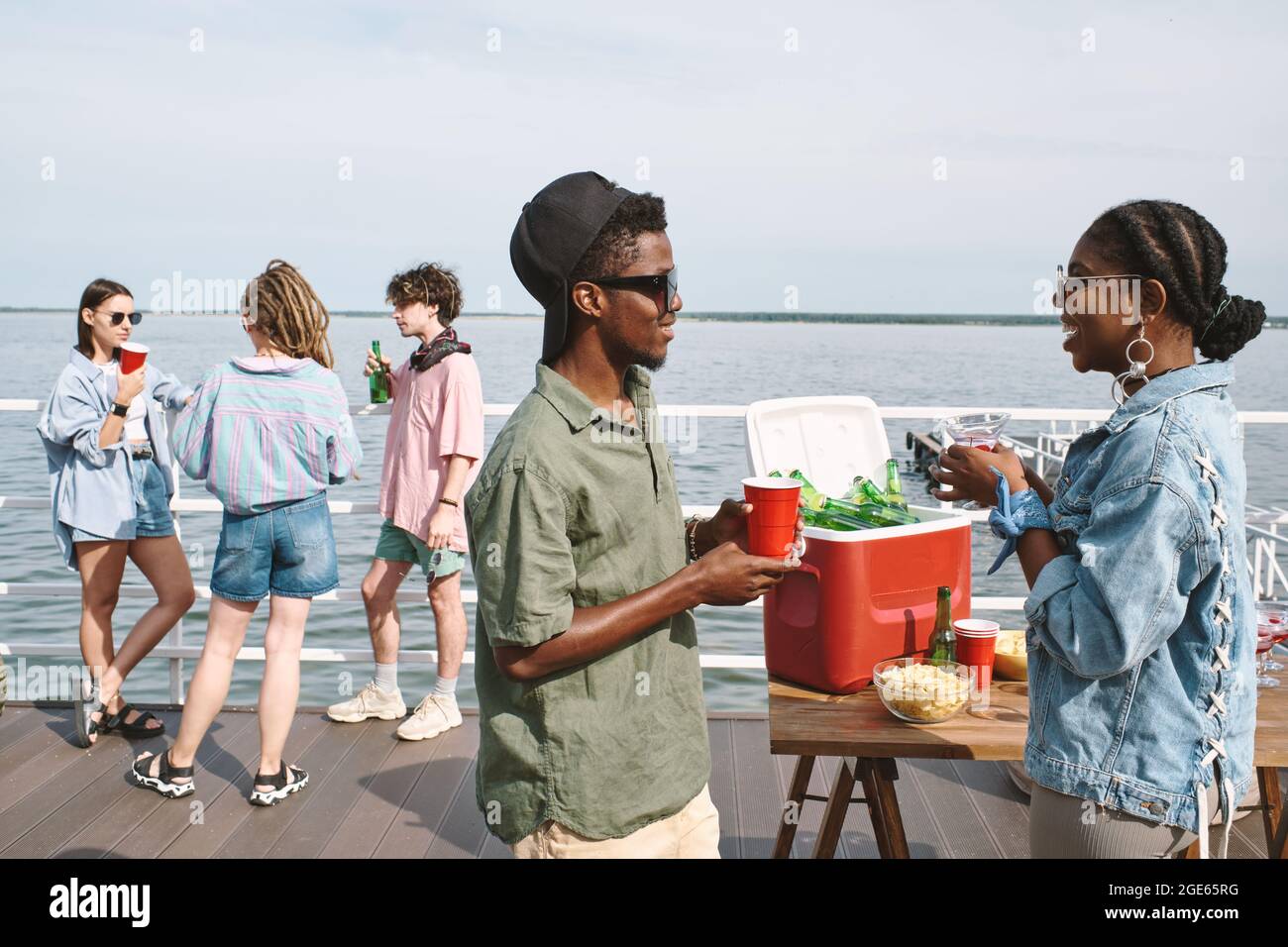 Junge Männer und Frauen flirten und scherzen auf der Party am Pier am See herum Stockfoto
