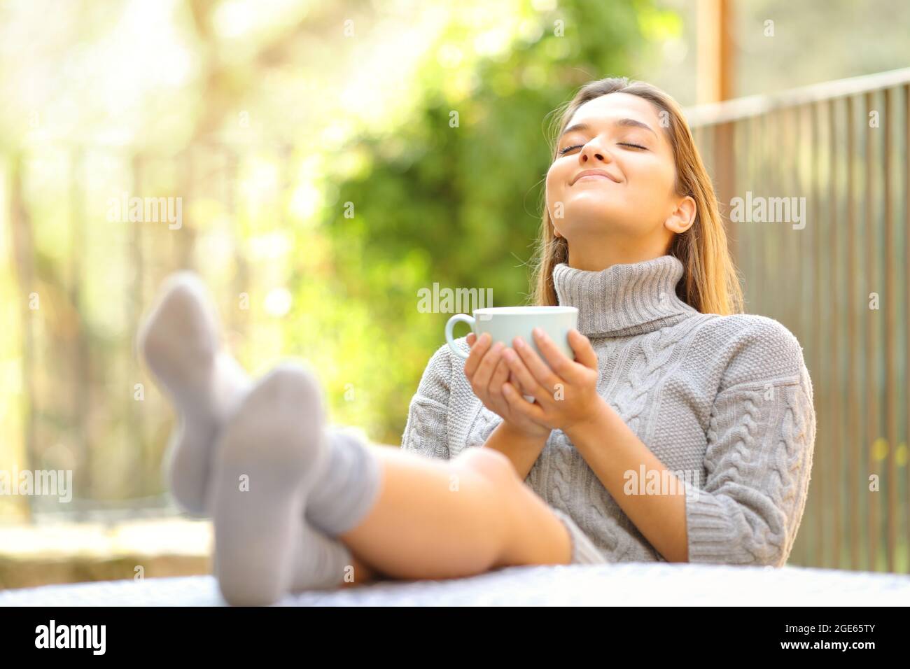 Unbeschwerte Frau, die frische Luft atmet und im Winter in einem Garten zu Hause Kaffee trinkt Stockfoto