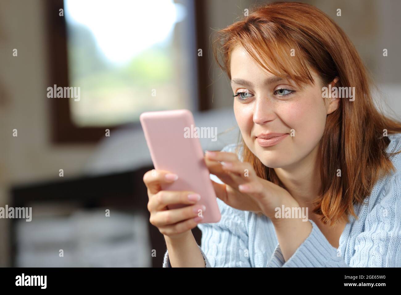 Eine zufriedene Frau, die zuhause im Schlafzimmer nach einem Smartphone gesucht hat Stockfoto