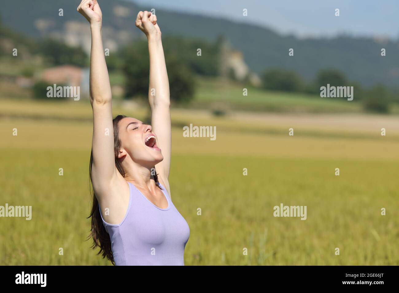 Aufgeregte Frau, die die Arme hebt und schreit und Sommerferien in einem Weizenfeld feiert Stockfoto