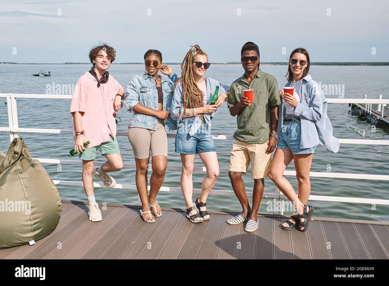 Eine Gruppe von glücklichen Freunden, die auf einem hölzernen Pier mit erfrischenden Getränken stehen, als sie eine kleine Party feiern Stockfoto