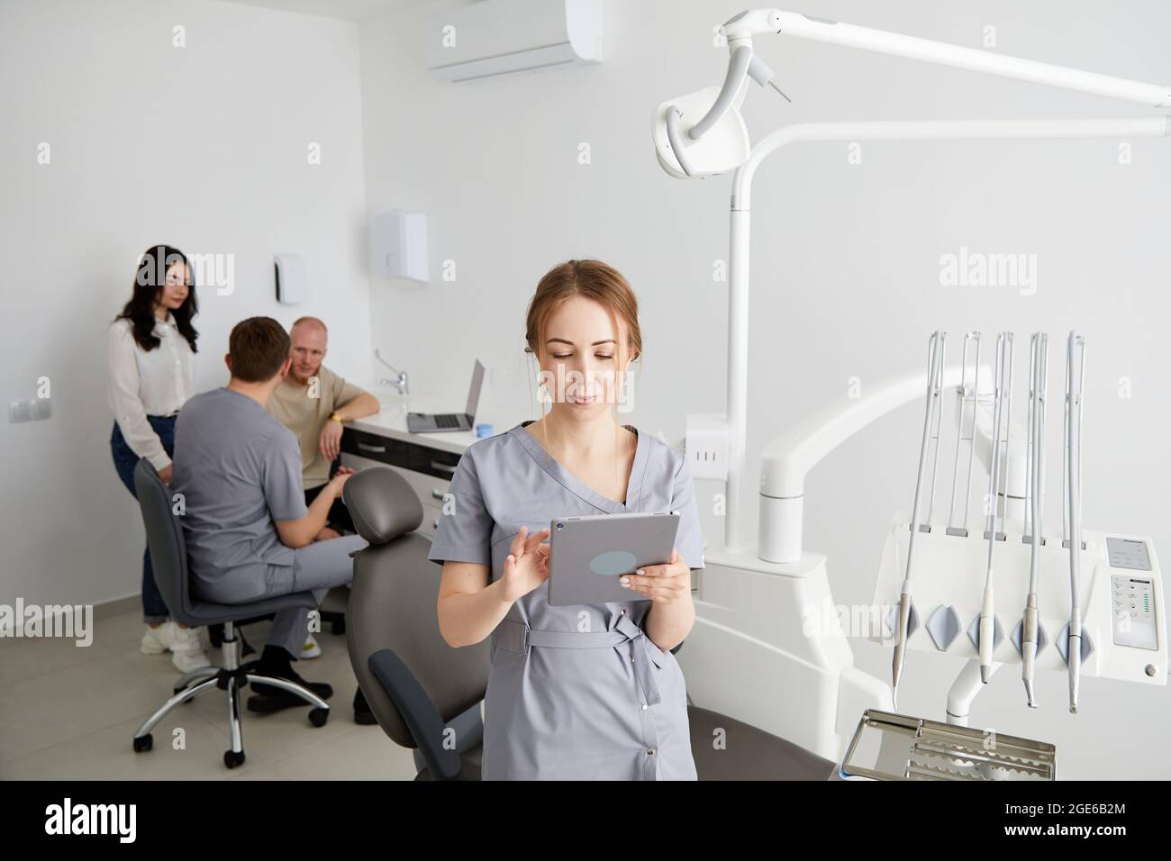 Mitten im Büro steht eine junge hübsche Zahnärztin, im Hintergrund berät eine Kollegin Patienten. Vorbereitung auf die Aufnahme von Stockfoto