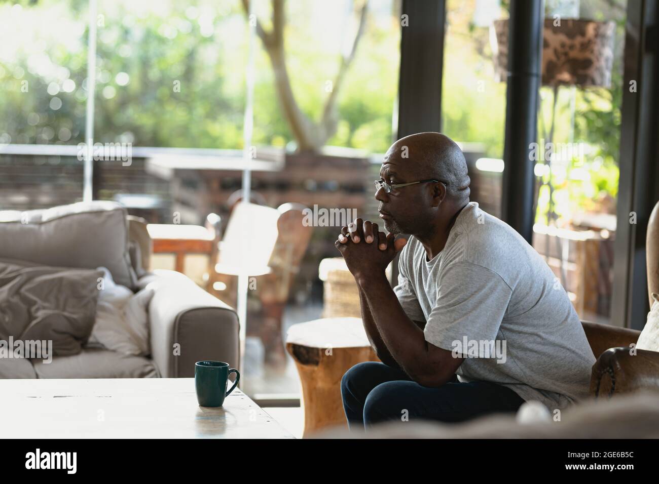 Nachdenklicher afroamerikaner mit gefalteten Händen auf der Couch sitzender Mann Stockfoto