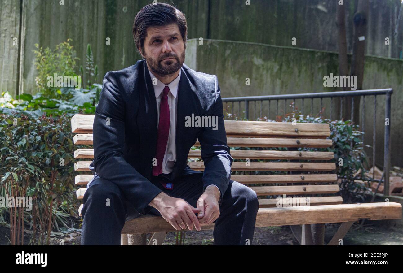 Mann in einem schwarzen Anzug und einer roten Krawatte, der jemanden in den Park sieht Stockfoto