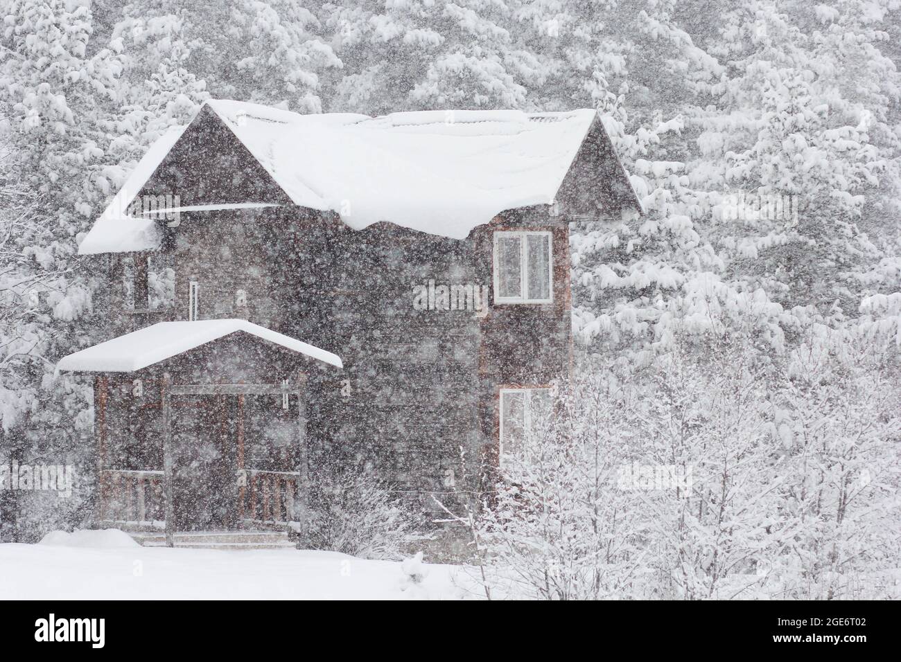 Zweistöckiges Holzhaus mit schneebedecktem Dach im Winterwald, verwischt durch Schneeflocken auf Schneeverwehungen Stockfoto