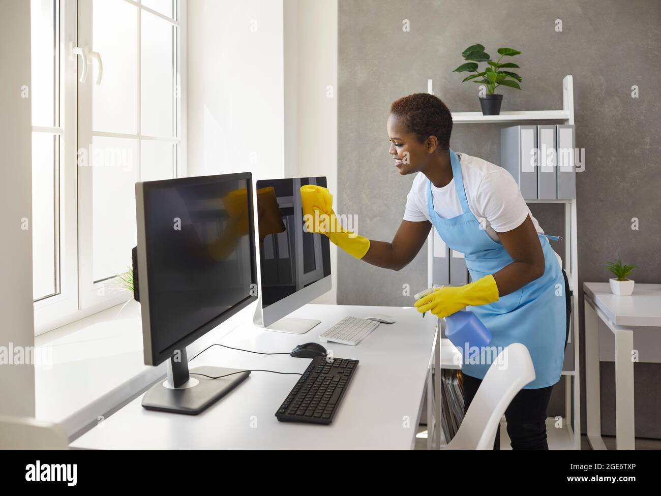 Glückliche Frau vom Reinigungsservice, der Computerbildschirme im modernen Büro abwischt Stockfoto