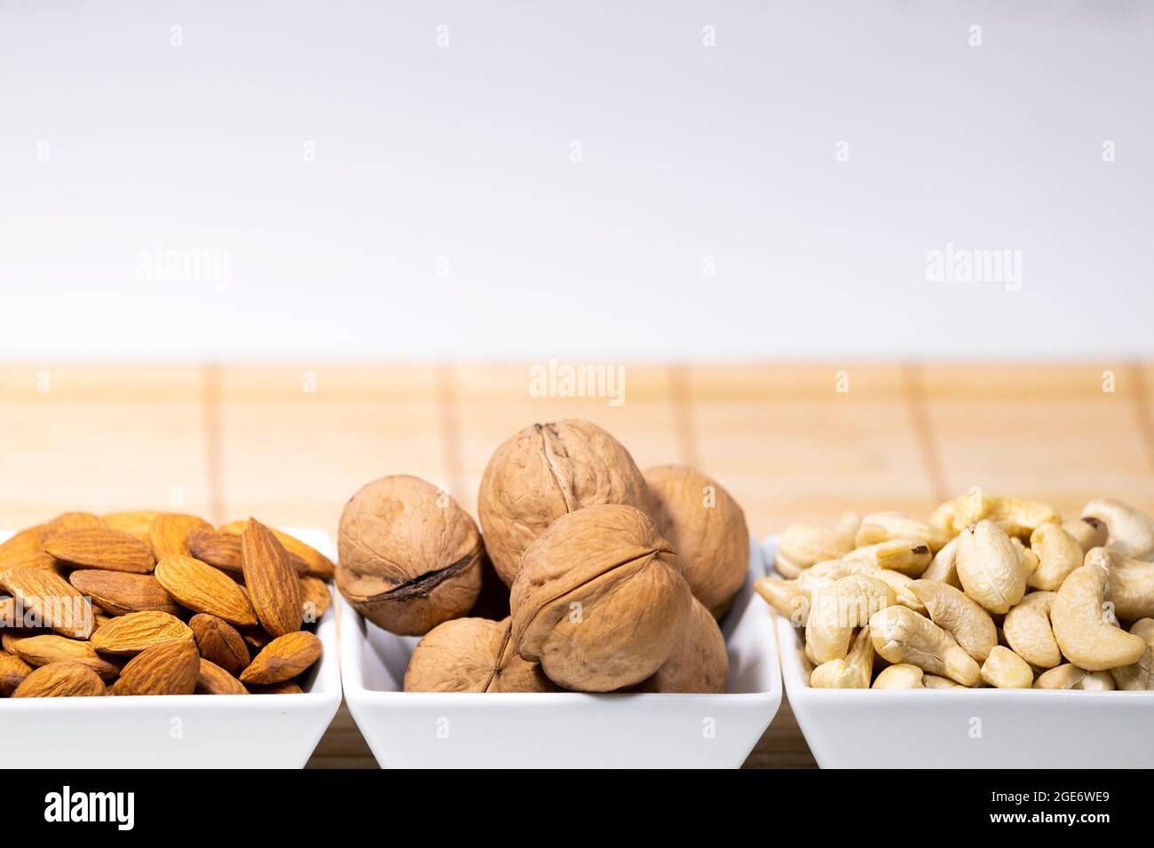 Mischung aus Nüssen, Mandel, Cashew, Wallnut in weißen Keramikschalen auf Holzständer, gesunde Snacks, Diät, Copyspace Stockfoto
