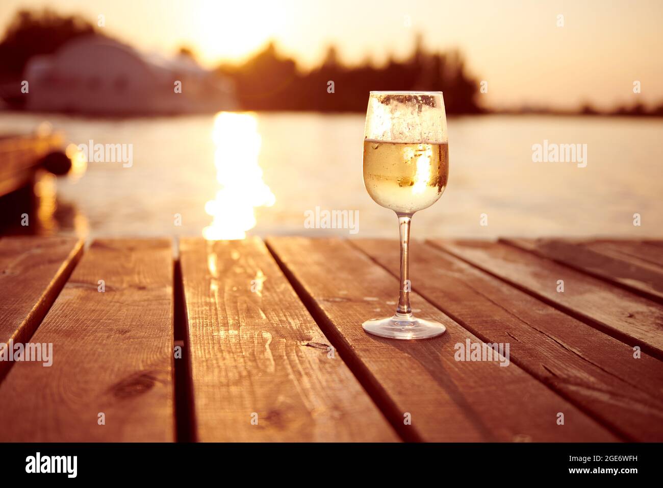 Weißwein in einem Sektglas bei Sonnenuntergang. Sekt auf einem hölzernen Pier. Single Drink mit warmem Licht. Entspannungskonzept Foto. Stockfoto