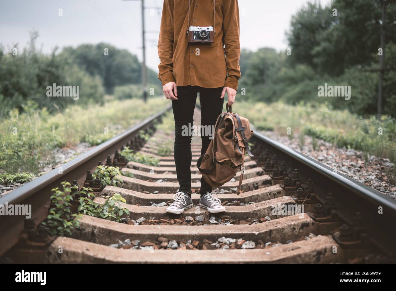 Fotograf in brauner Jacke mit Rucksack und Retro-Kamera auf der Eisenbahn Stockfoto