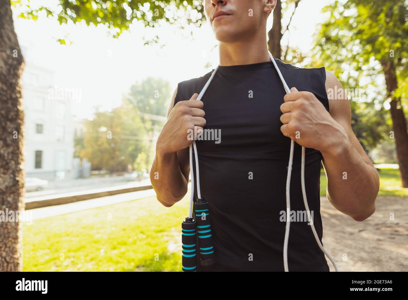 Ein junger, hübscher kaukasischer Mann in Sportkleidung, der am hellen Sommertag mit Seil auf dem Sportplatz posiert. Stockfoto