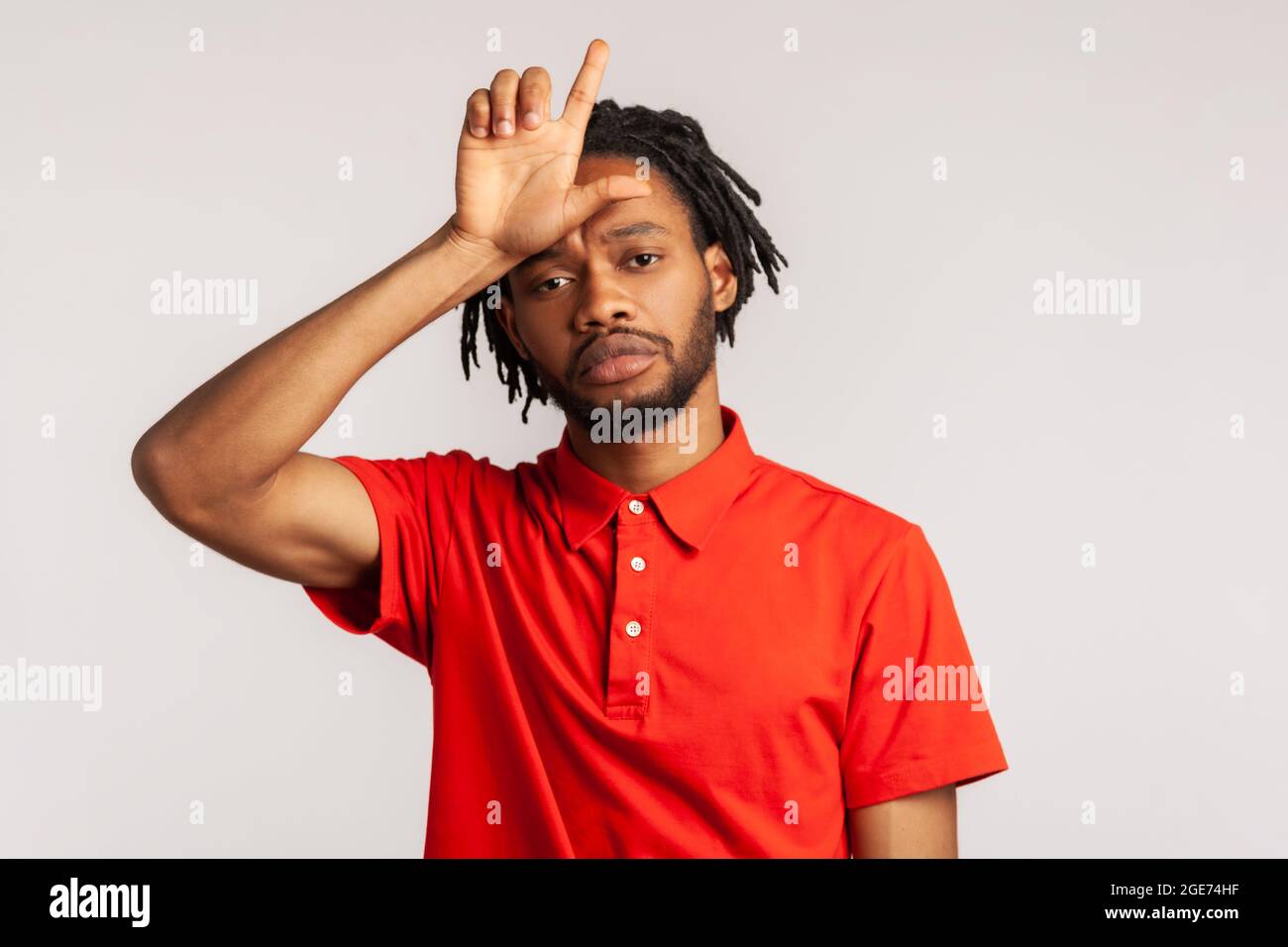 Ein hübscher Mann mit Dreadlocks trägt ein rotes T-Shirt im lässigen Stil und zeigt eine lockere Geste, die die Finger an die Stirn hält, traurig wegen eines dummen Fehlers. Ind Stockfoto