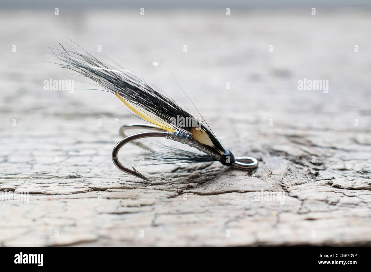 Glänzende Lachsfischfliege mit gelbem Blitz auf einer Holzoberfläche Stockfoto