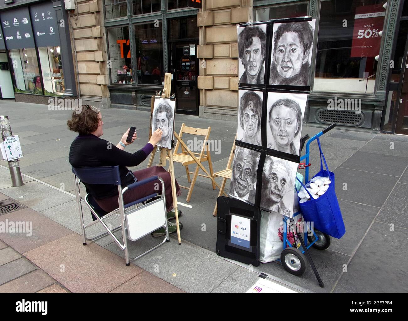 Eine Straßenkünstlerin in der Buchanan Street in Glasgow zeichnet einige Porträts bekannter Menschen, um die Öffentlichkeit dazu zu ermutigen, für sie zu sitzen und zu posieren. Stockfoto