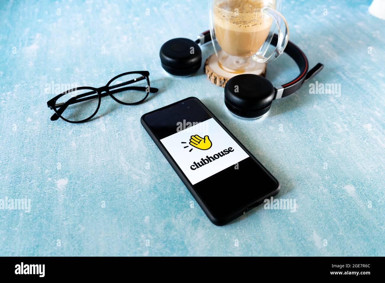 Flatlay-Aufnahme des Mobiltelefons mit der Clubhouse Audio Only Social Media App mit Brillenkopfhörern und einem Kaffeebecher gefüllt mit Dalgona Stockfoto