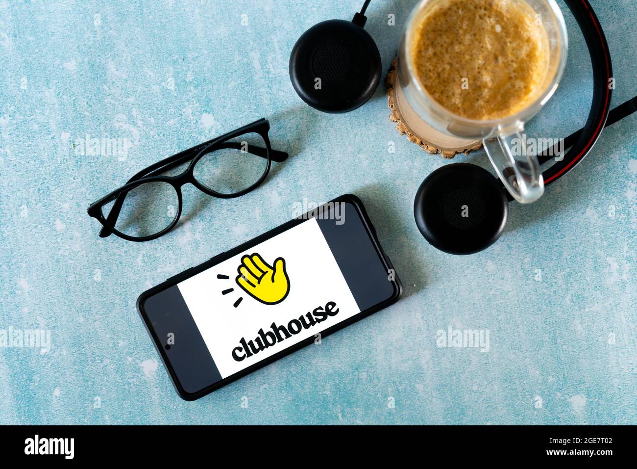 Flatlay-Aufnahme des Mobiltelefons mit der Clubhouse Audio Only Social Media App mit Brillenkopfhörern und einem Kaffeebecher gefüllt mit Dalgona Stockfoto