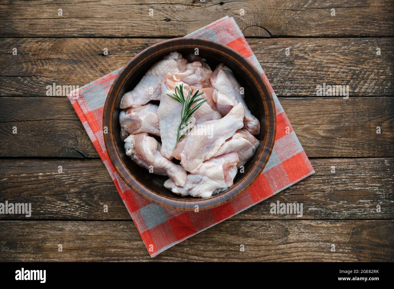 Rohe Hähnchenflügel in der Schüssel zum Kochen vorbereiten. Frische, ungekochte Drumette oder Drumstick mit Rosmarin zum Grillen und grillen auf dem Holzhintergrund. Roh Stockfoto