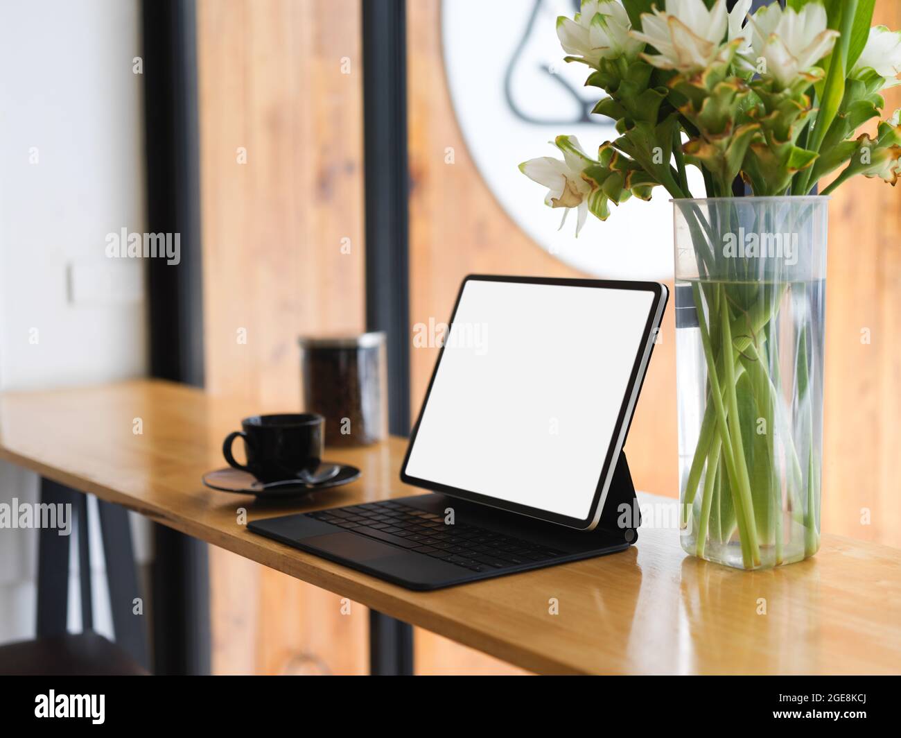 Tragbarer Arbeitsplatz mit tragbarem leerem Tablet-Bildschirm-Modell mit magischer Tastatur, Kaffeetasse, Blumen in Glasvase auf Holztisch Stockfoto
