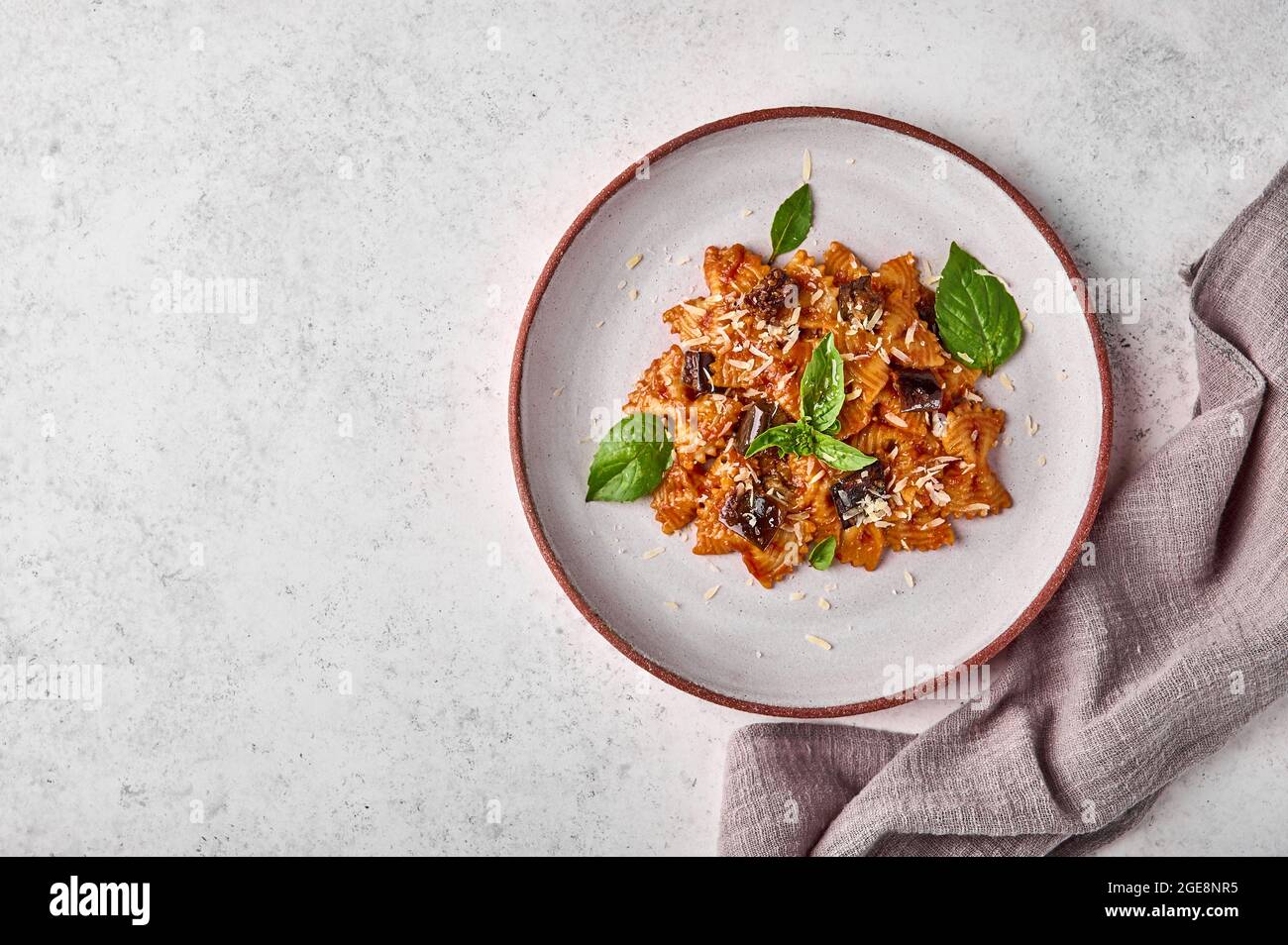 Farfalle Pasta mit Auberginen, Tomatensauce und Basilikum auf Teller mit Serviette auf grauem Hintergrund, flaches Lay, Kopierraum Stockfoto