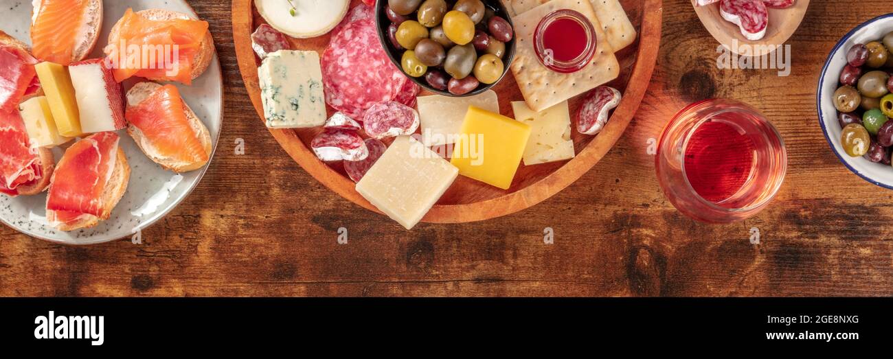 Panorama aus Wurstwaren und Käseplatten mit Rosenwein, Oliven und einem Platz für Text, aufgenommen von oben auf rustikalem Hintergrund. Spanische Tapas oder italienische Antipasti Stockfoto