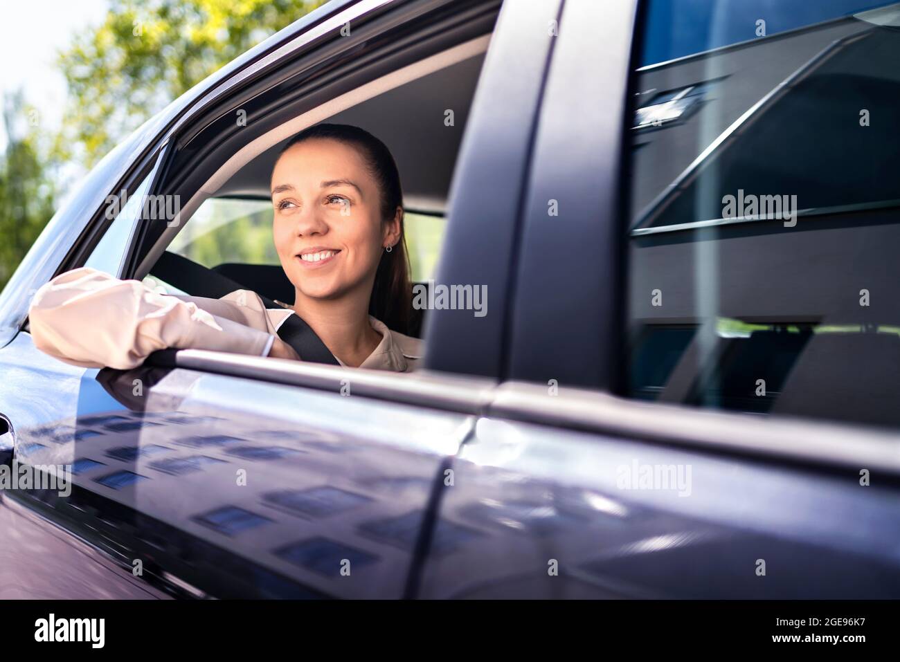 Frau im Auto als Beifahrer auf dem Rücksitz. Lächelnde Kundin im Taxi, die aus dem Fenster schaute. Glückliche elegante Geschäftsfrau. Stockfoto