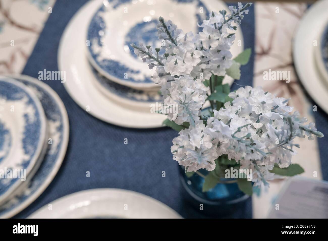 Einstellung des Stilllebenstabs. Vase mit Blumen, Kerzen, blauer Tischdecke, schönen Tellern. Tischdekoration Stockfoto