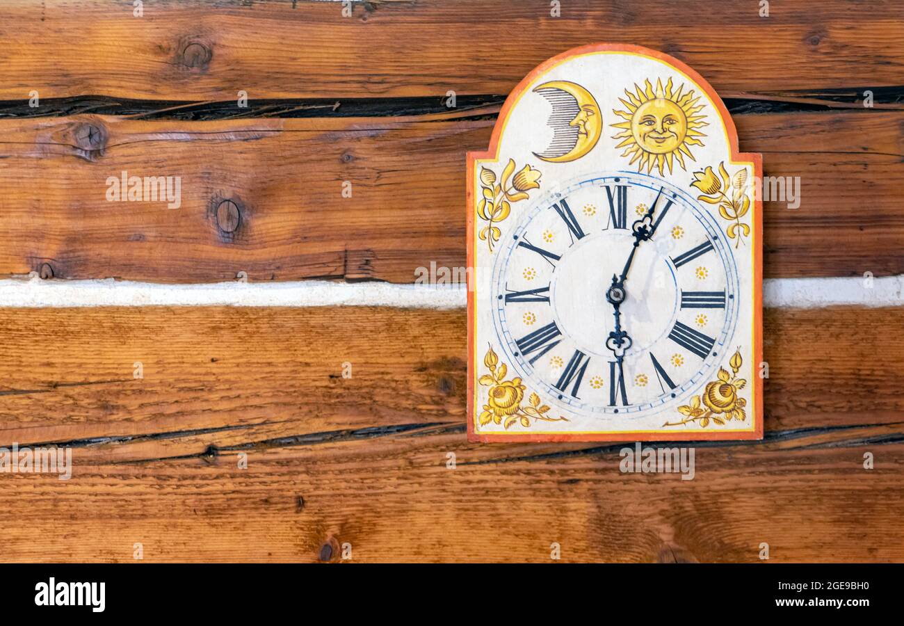 Die alte Uhr mit Bildern, die an einer Wand aus Holzbalken hängen. Stockfoto