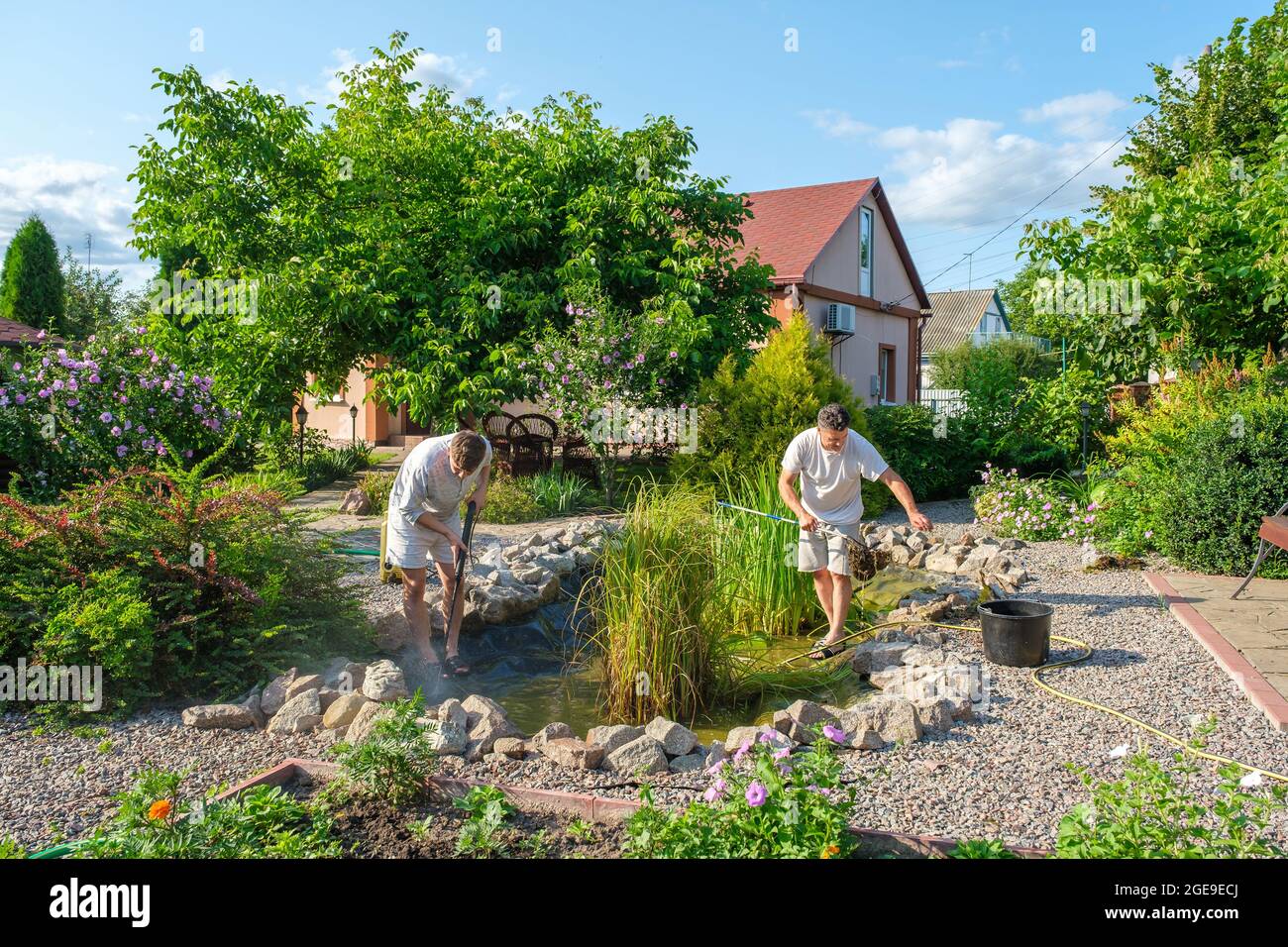 Vater und Sohn putzen Gartenteichboden mit Hochdruckreiniger vom Schlamm Stockfoto