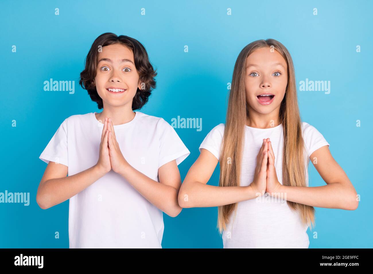 Foto von zwei fröhlichen Kindern halten Hände pliad aufgeregt Stimmung tragen weißen T-Shirt isoliert blauen Hintergrund Stockfoto