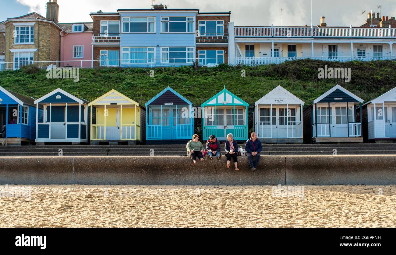 Vier Personen sitzen auf der Promenade mit Strandhütten hinter sich in Southwold in Suffolk in England. Stockfoto